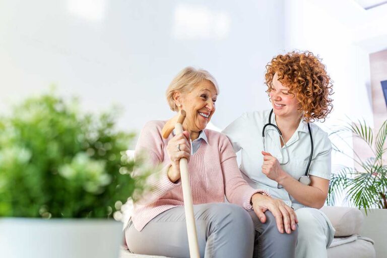 Family members visit an older adult in a bright assisted living room with photos and refreshments.